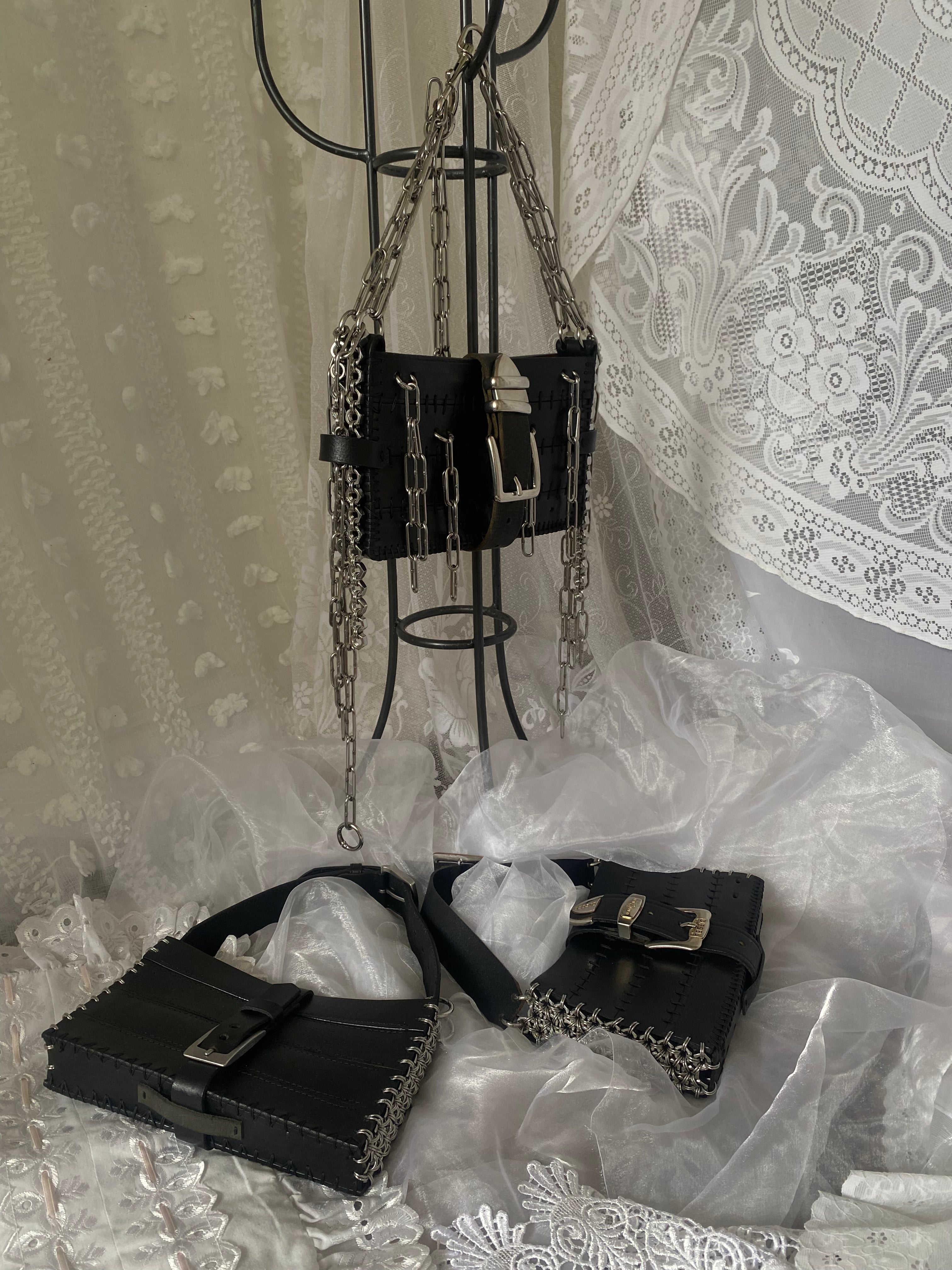 Three sustainable black handbags made from upcycled leather with unique chainmail and stainless steel chain details, displayed on a Victorian gothic lace fabric.