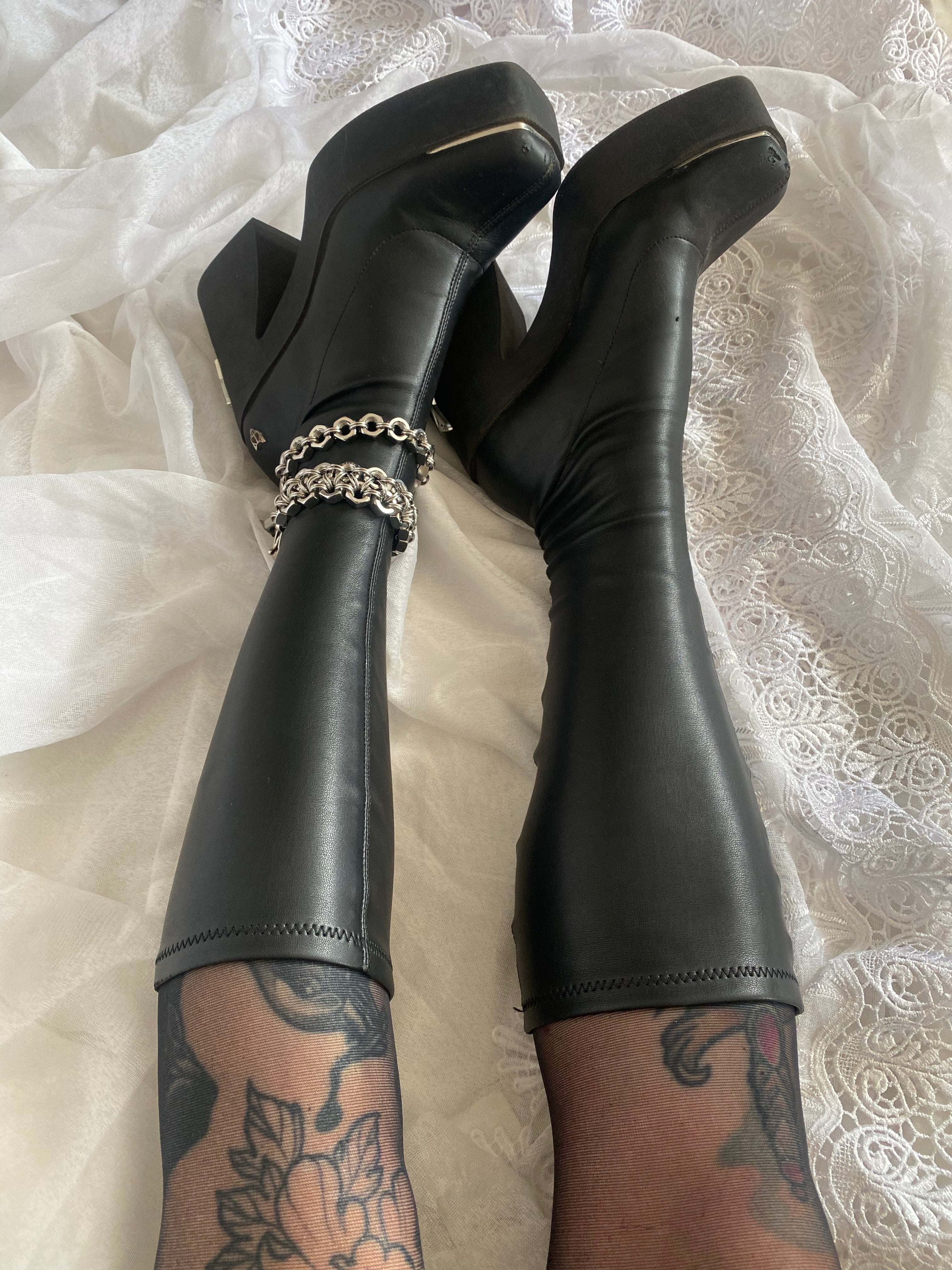 Industrial stainless steel boot charm made from authentic screws and chainmail, displayed on Naked Wolfe knee-high boots worn on a tattooed leg. Perfect for alternative fashion lovers.