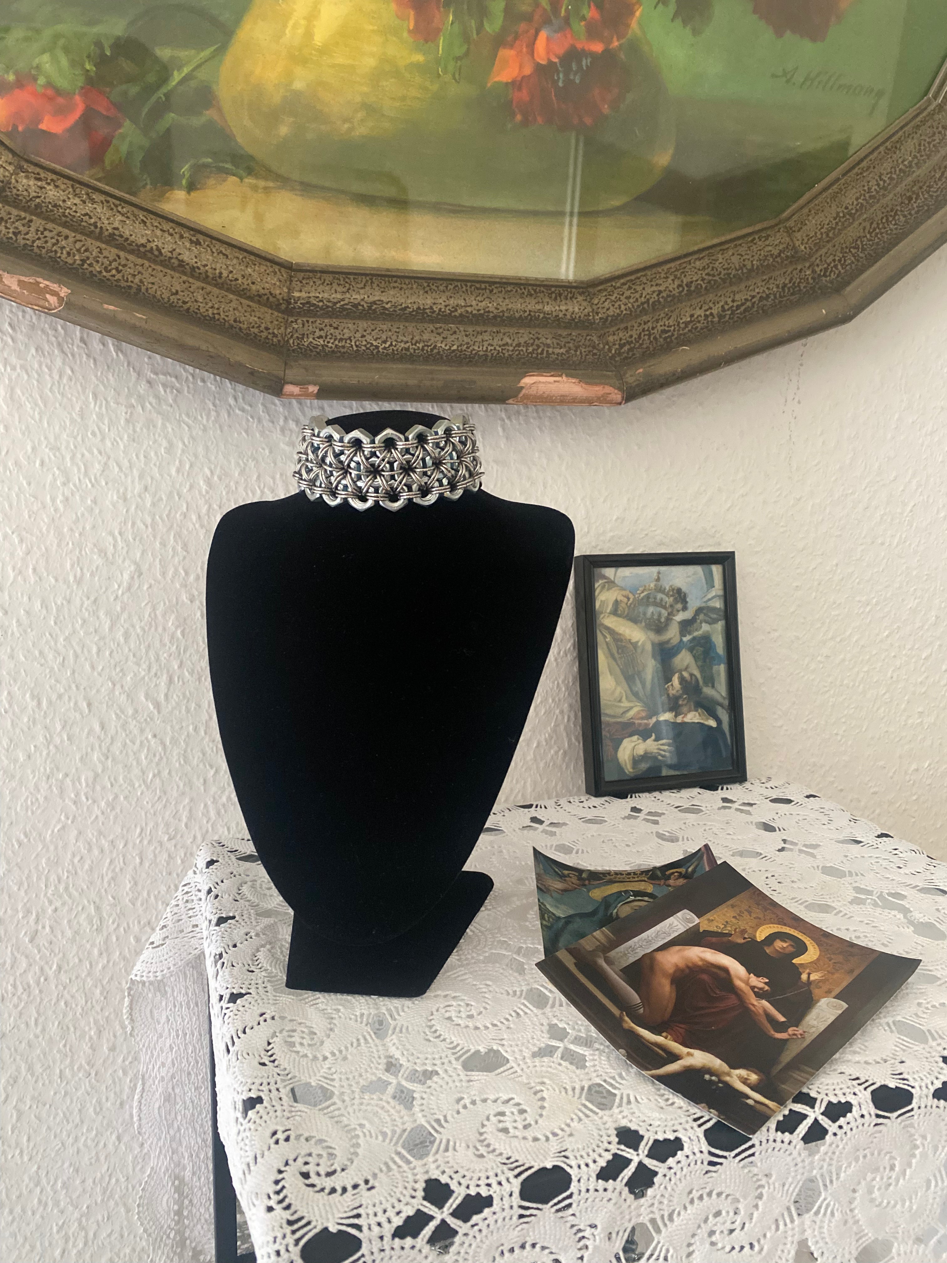 Heavy-duty chainmail-inspired choker made from stainless steel screws and chainmail, presented on a doll wearing white lace for a gothic lookbook, set in front of a vintage rose painting.