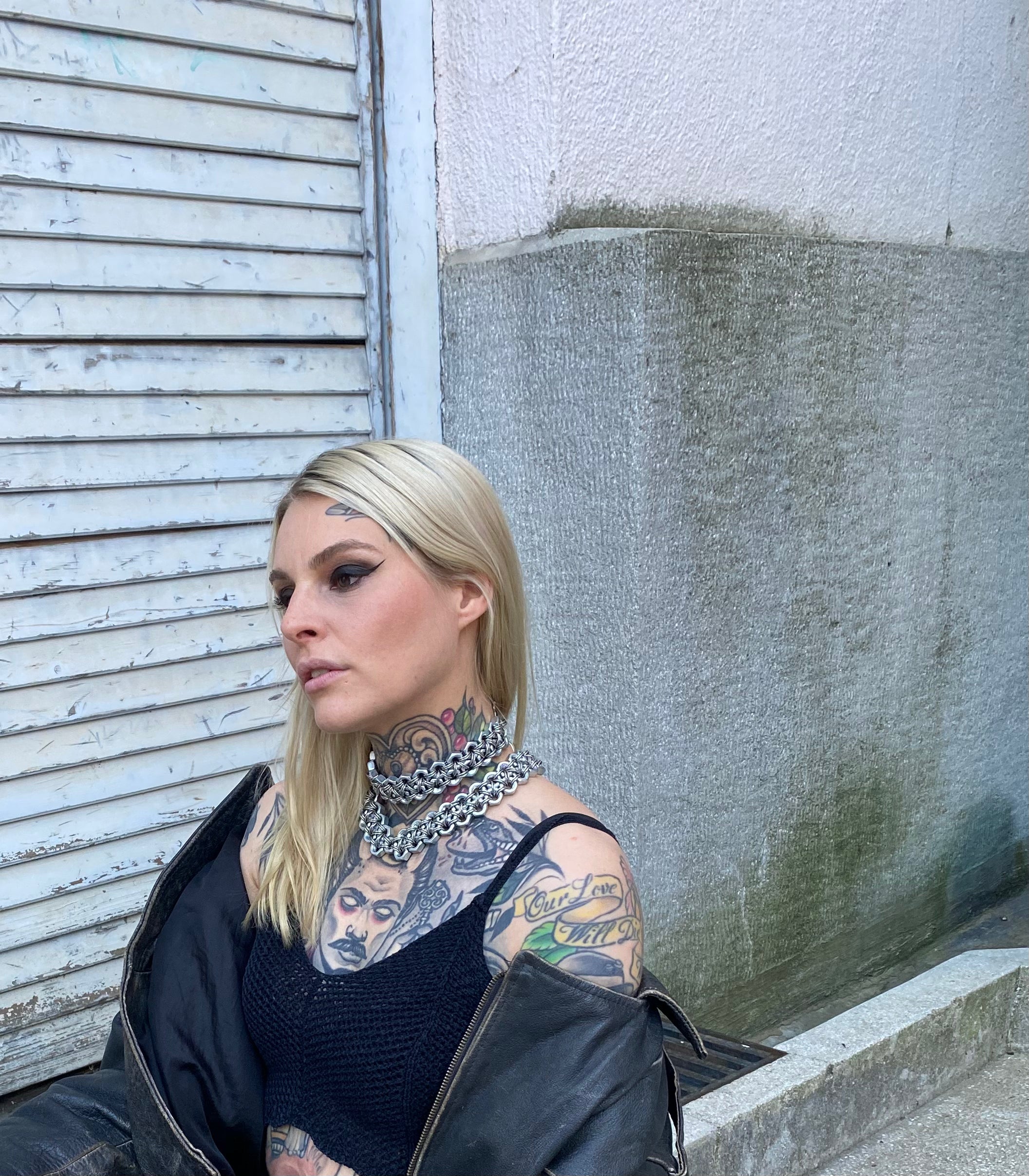 Tattooed model wearing industrial heavy-metal chainmail choker necklaces made from stainless steel screws and chainmail, styled with a vintage leather jacket.