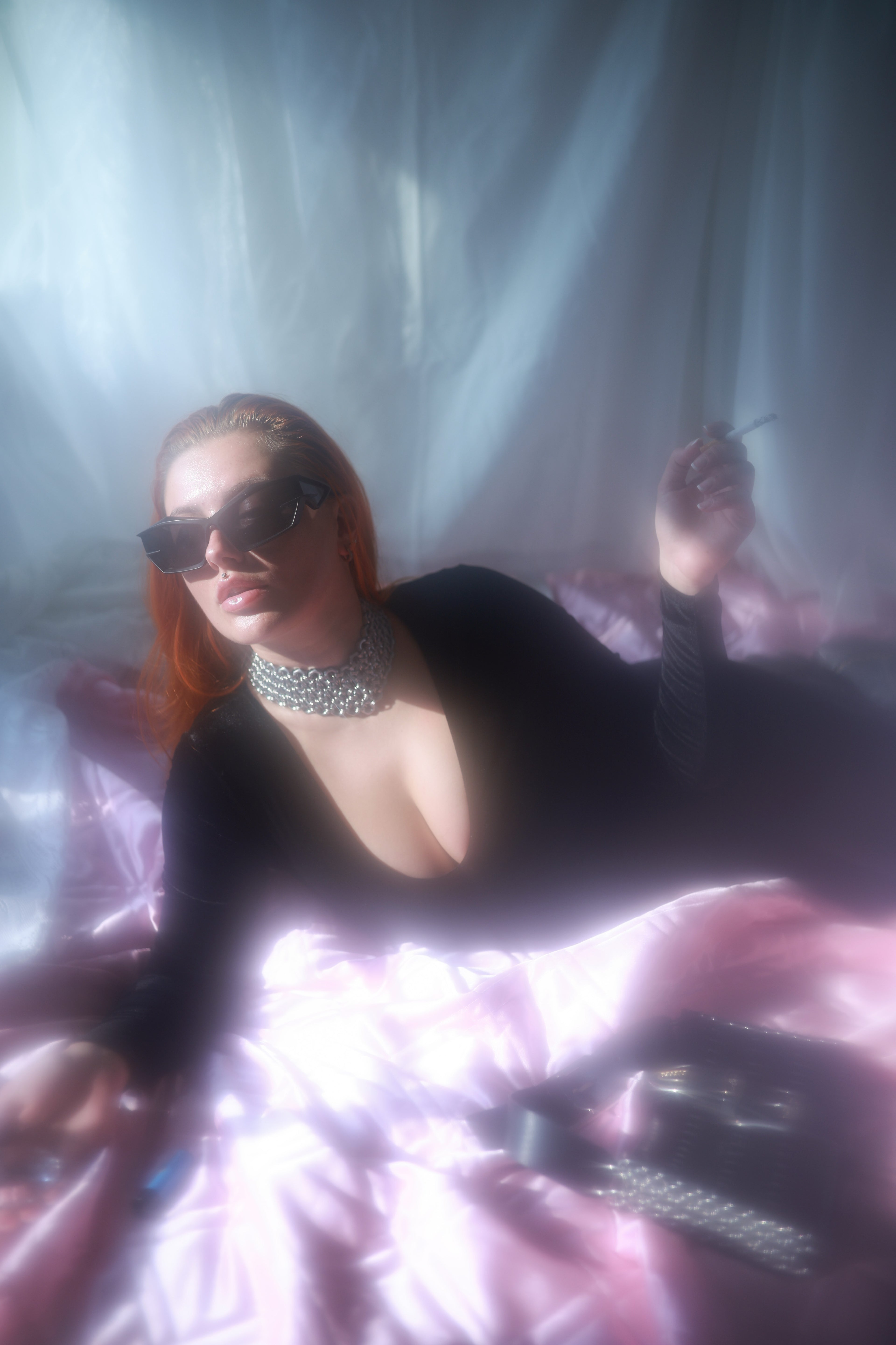Redhead model lying on a vintage bed, wearing a heavy-duty industrial full-neck choker necklace made from stainless steel screws and chainmail, handmade in Berlin; a silver-shining statement piece with a bold design for fashion enthusiasts.
