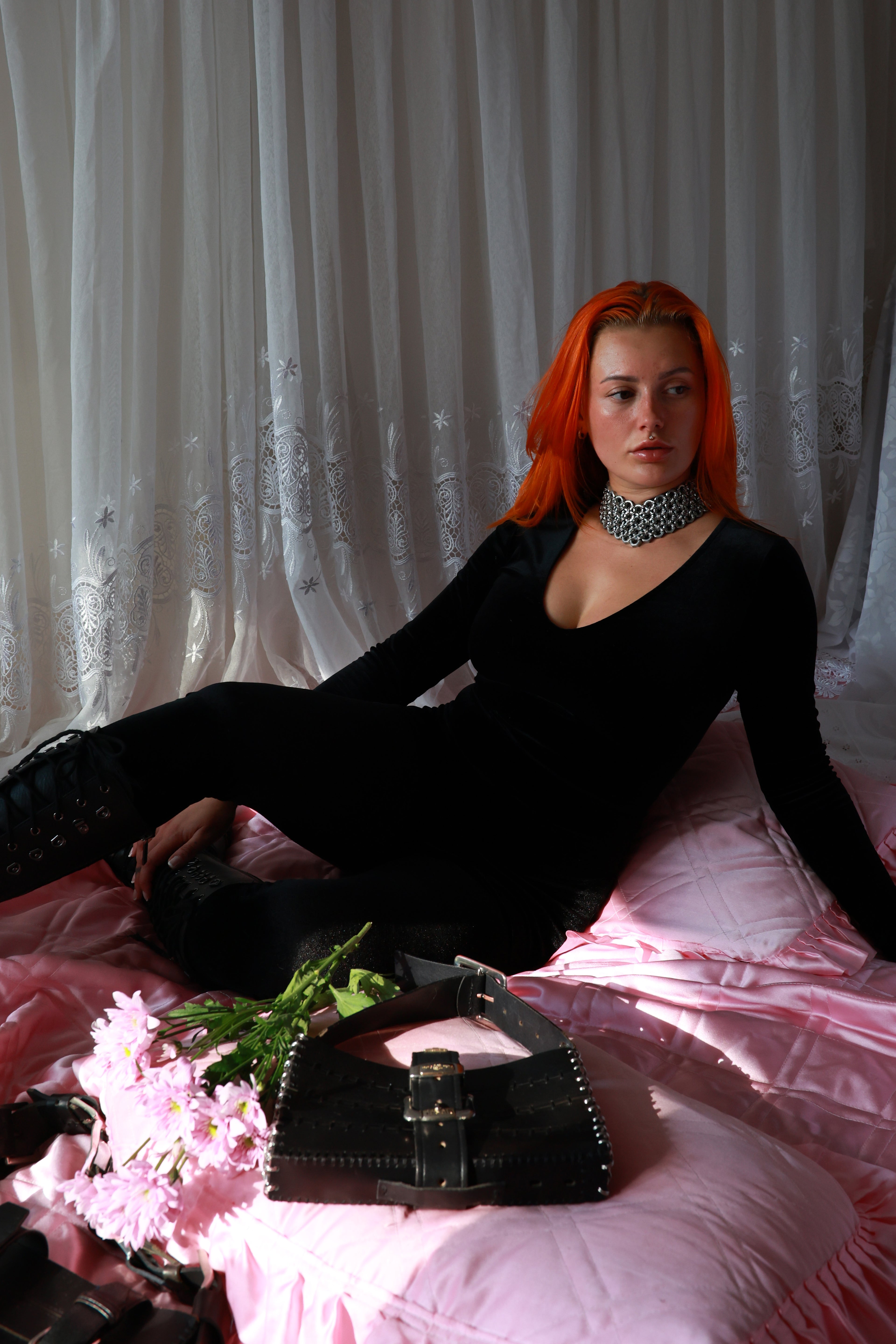 Model lying on a pink bed in a vintage-style room, wearing a heavy-duty metal chainmail choker made from stainless steel; an avant-garde statement piece for bold, fashion-forward individuals.