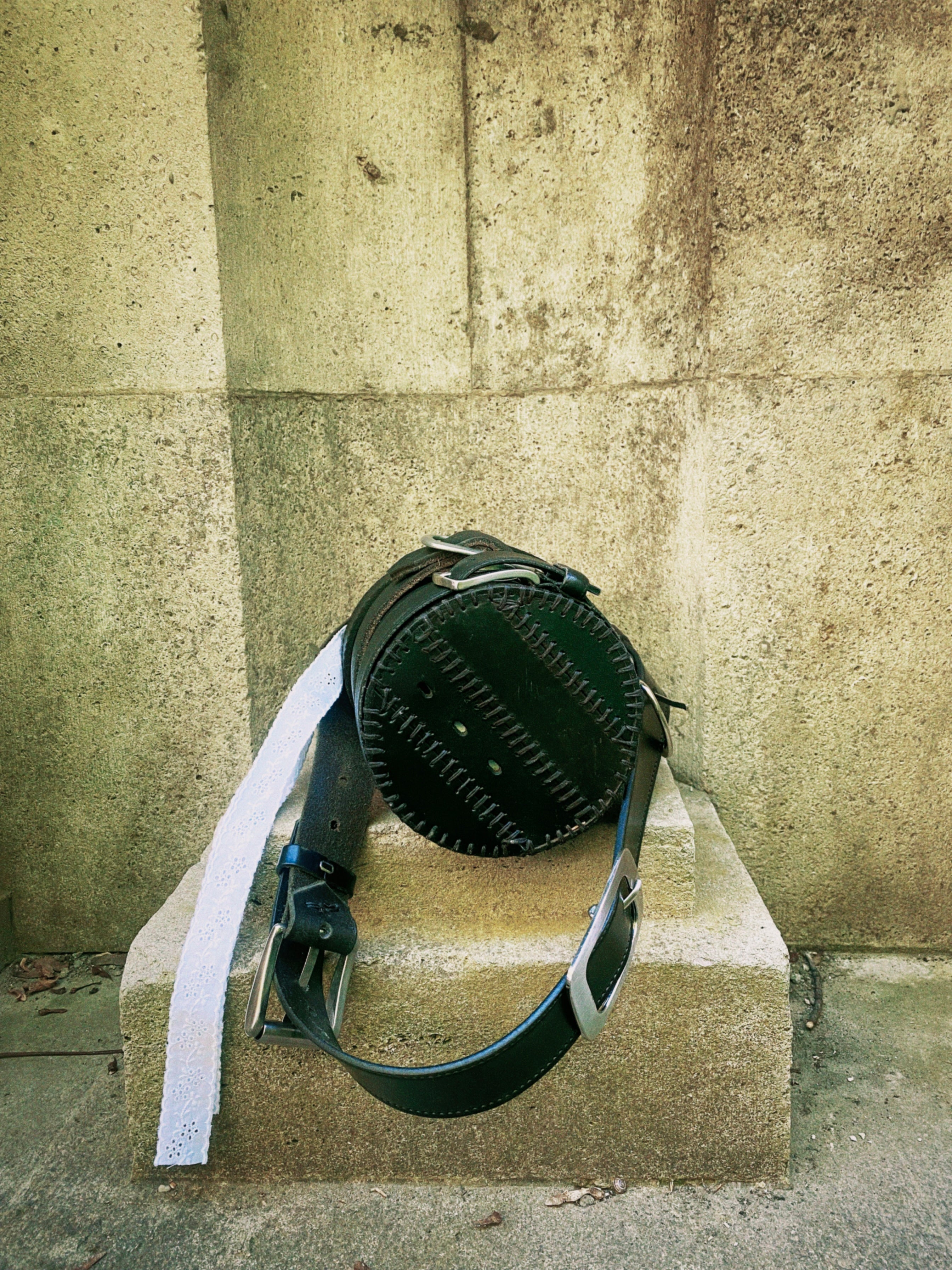 Cylinder-shaped sustainable handbag with hand stitching, belt buckles, and bold vegan-friendly design in repurposed leather.