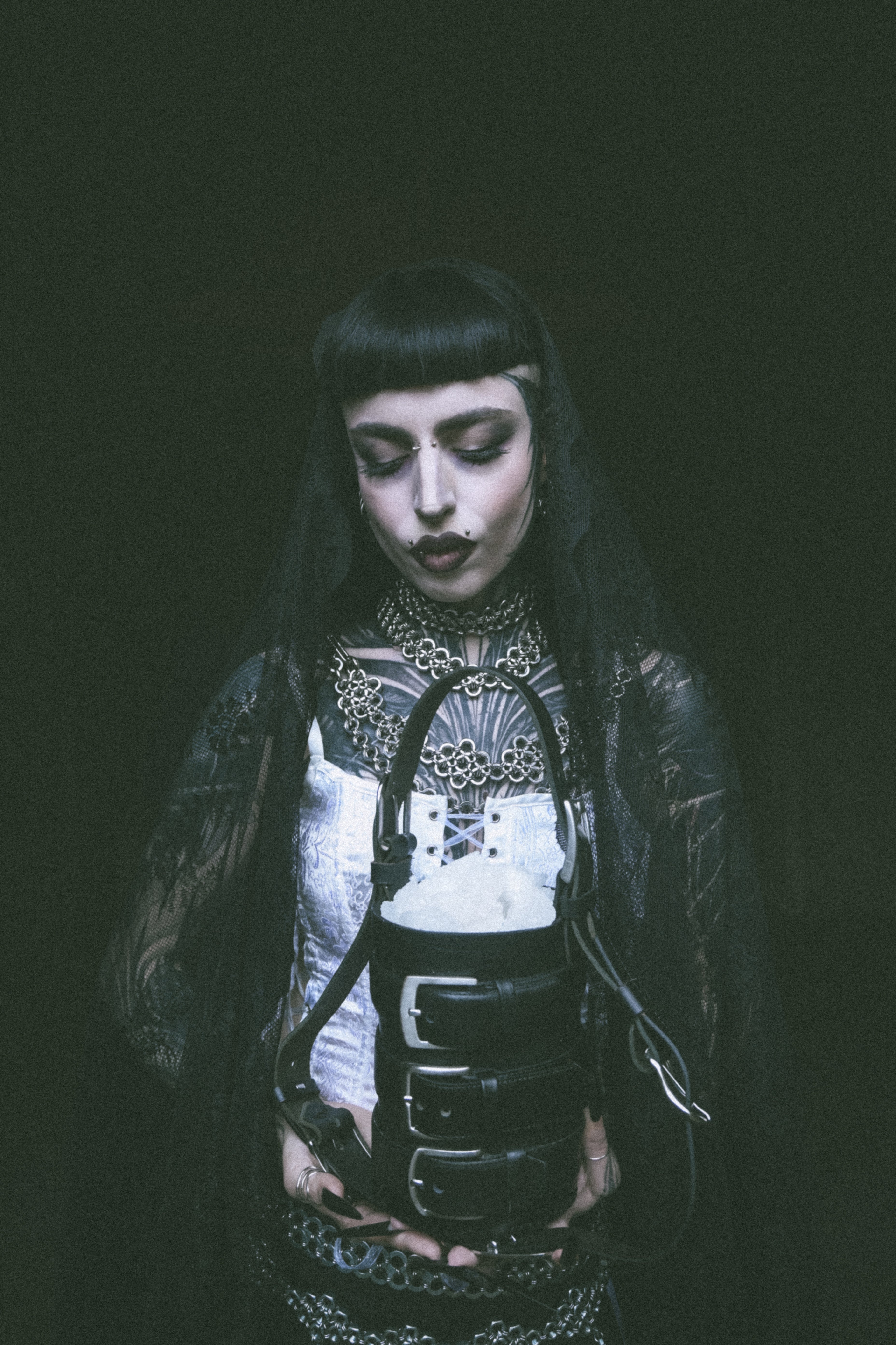 Alternative vampire-inspired model holding a cylinder-shaped sustainable handbag made from upcycled leather, featuring straps and three belt buckle closures.