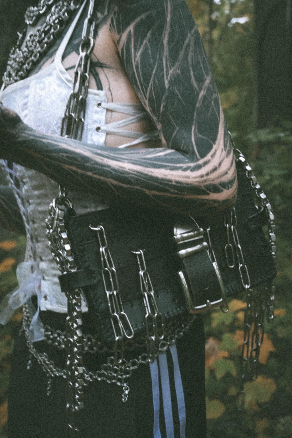 Alternative vampire-inspired model wearing a handmade shoulder bag made from repurposed leather with unique industrial chainmail details, photographed in an actual gothic graveyard.