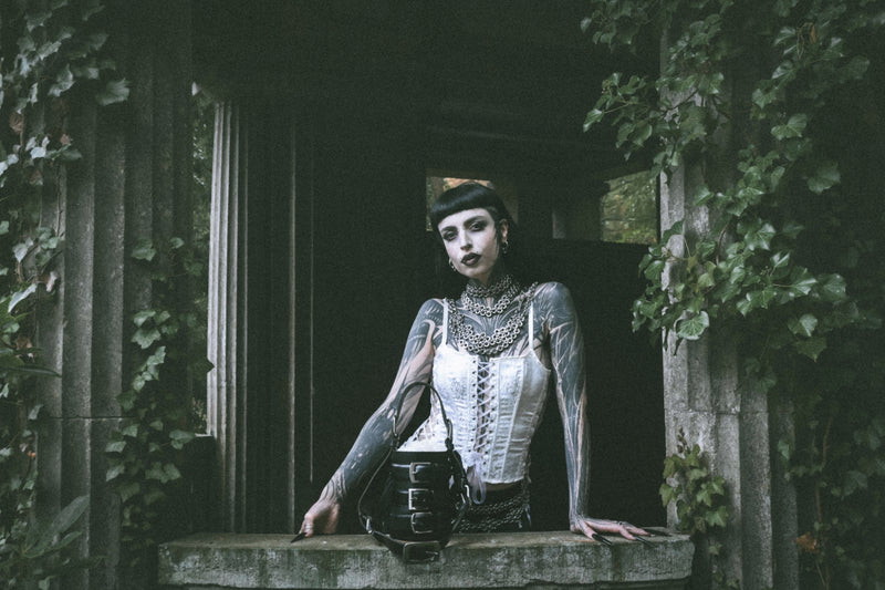 goth alternative model wearing sustainable leather handbag and chainmails in beautiful green enviroment with gothic buildings