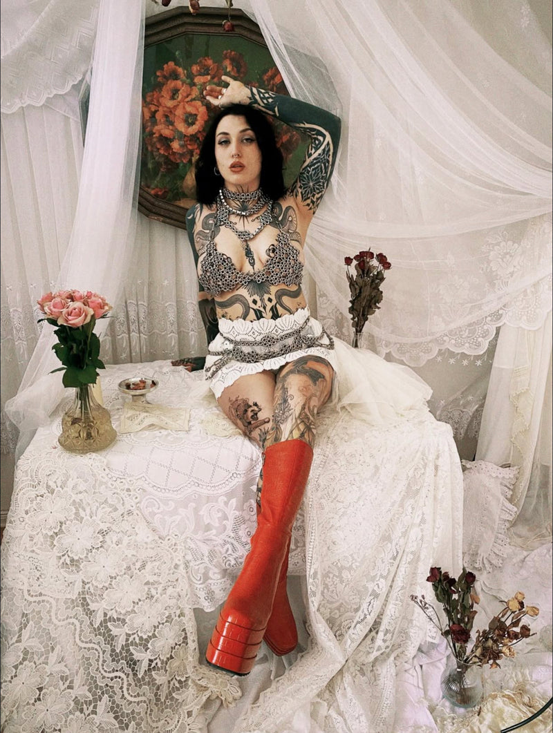 tattooed model wearing industrial chainmail set made from screws in front of gothic scenery
