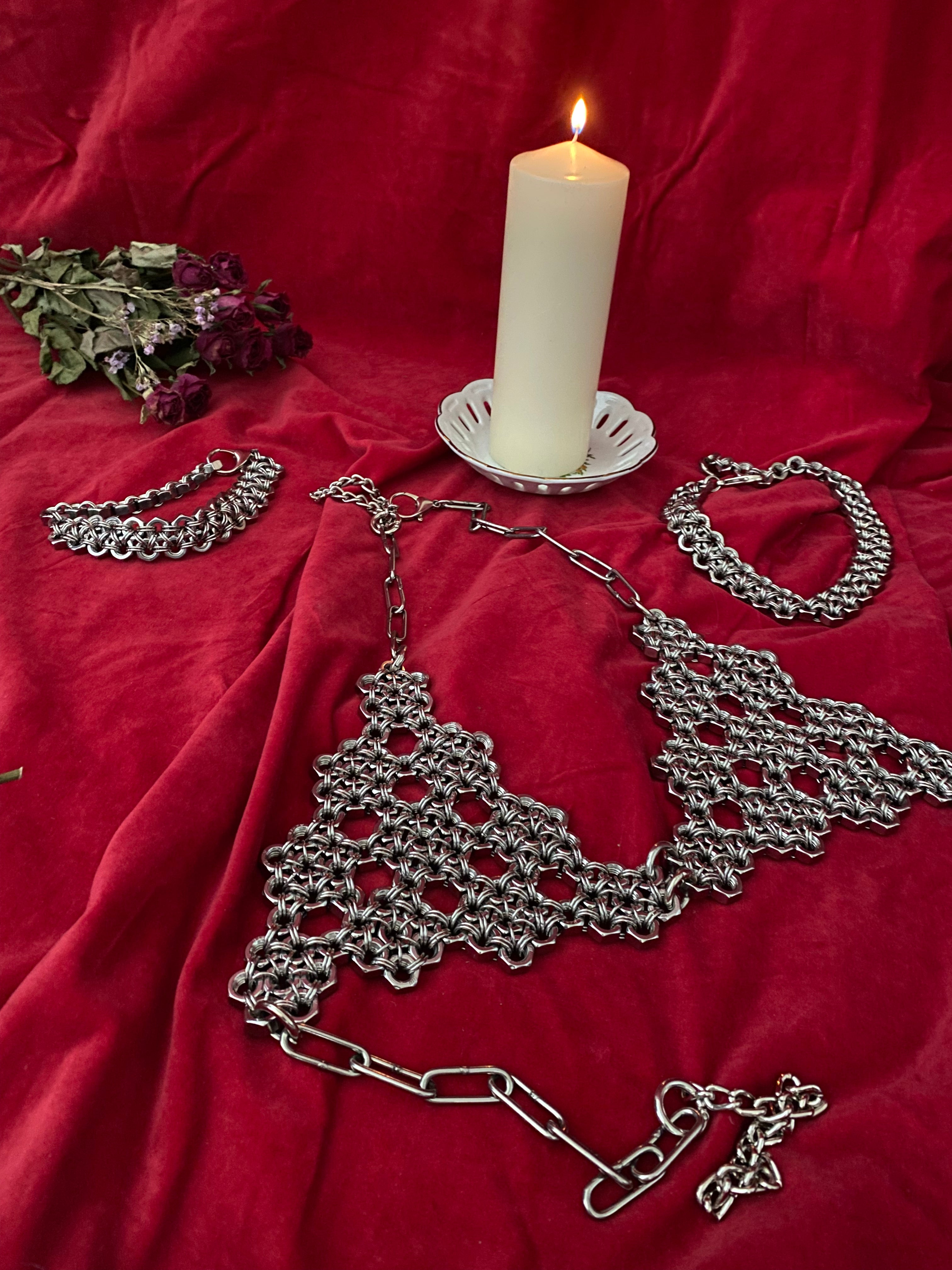 Handmade chainmail bra and top crafted from stainless steel rings and industrial screws, displayed on burgundy velvet fabric with candlelight, creating a gothic alternative fashion look. Made in Berlin.