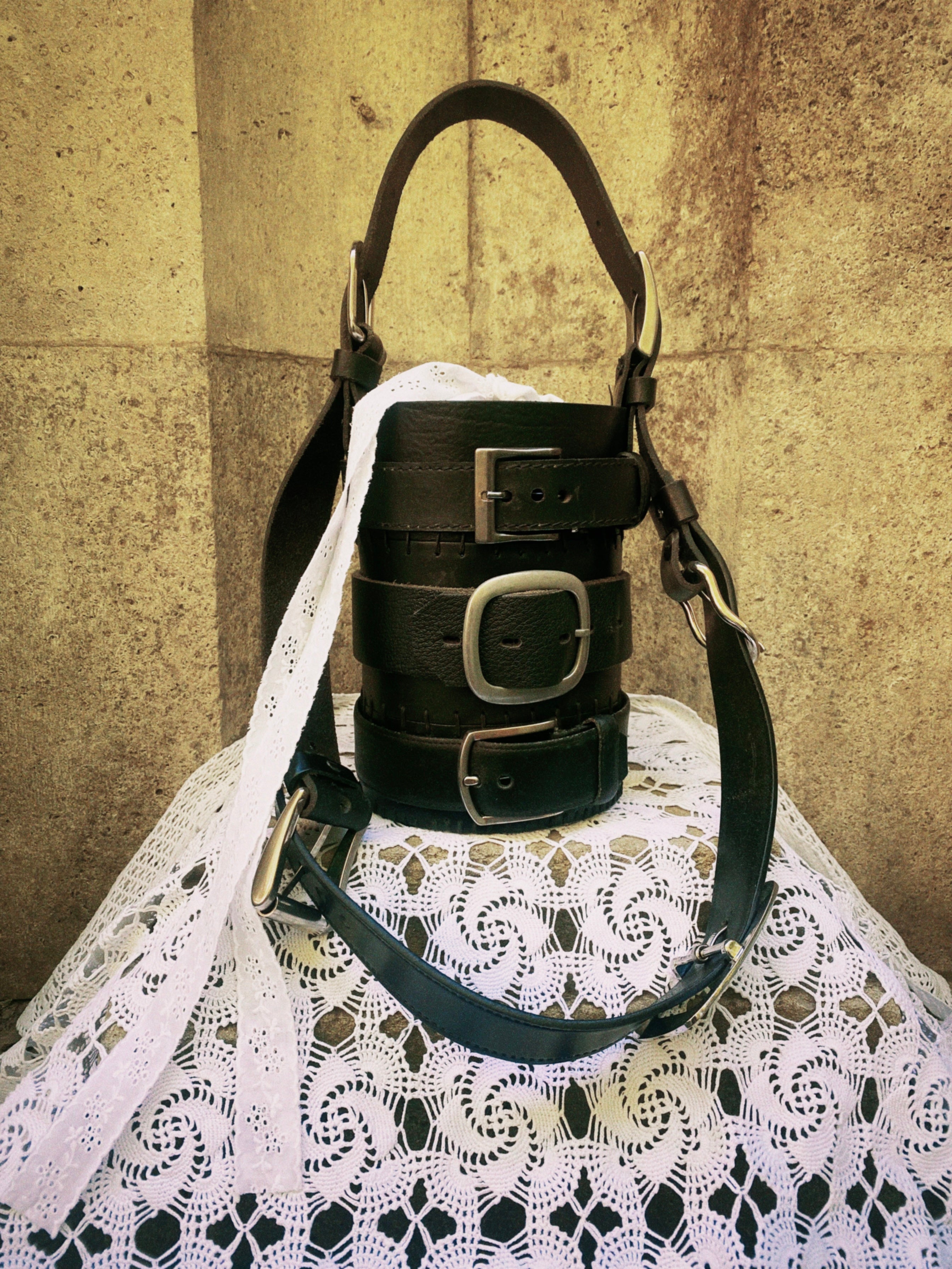 Cylinder-shaped black leather handbag made from repurposed leather and upcycled belt material, standing on a gothic-style rock surface. Bold statement design for fashion enthusiasts.