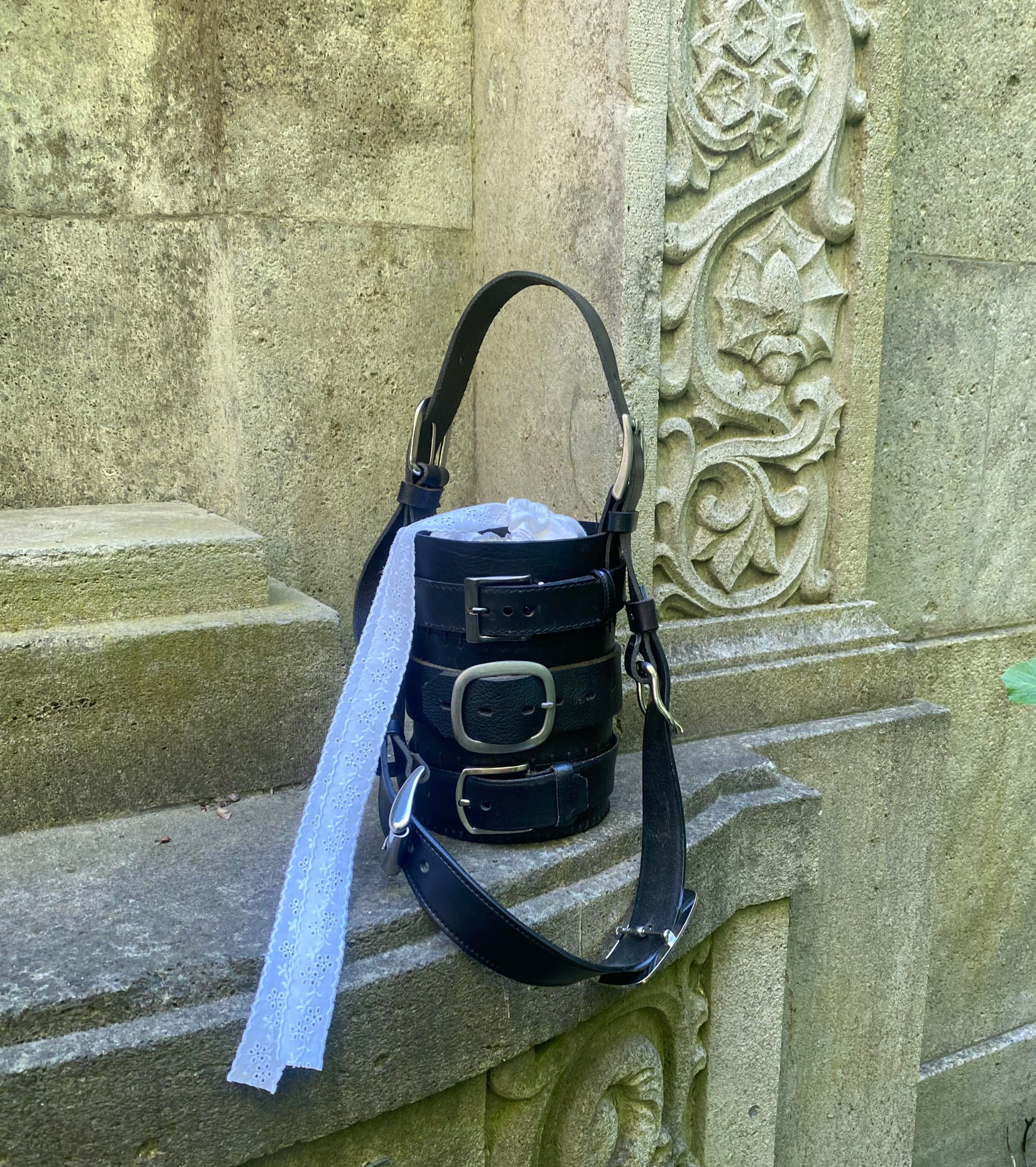 Cylinder-shaped black leather handbag with three stacked belts, made from sustainable upcycled leather. Alternative statement piece.