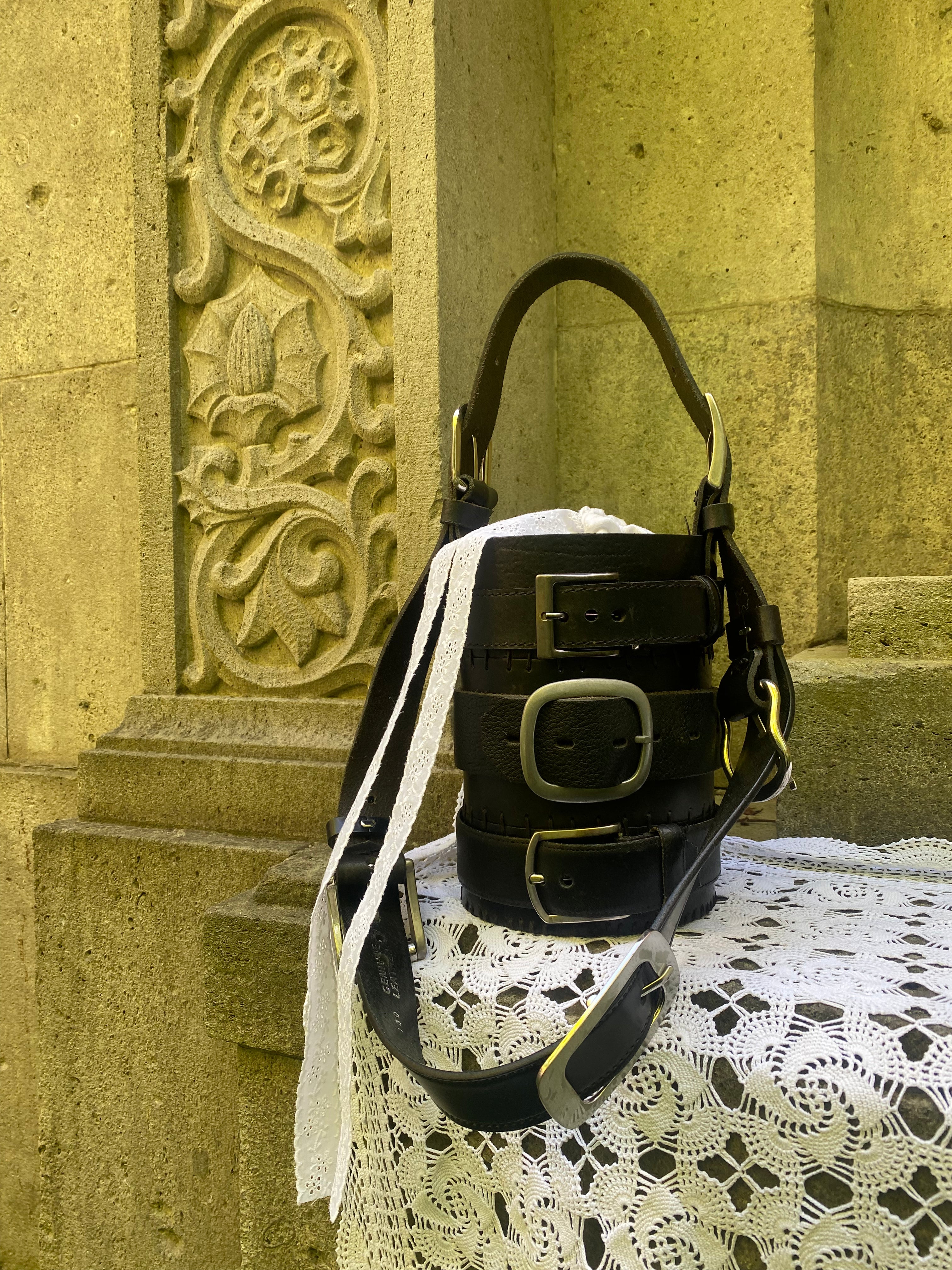 Cylinder-shaped black handbag from repurposed leather on gothic-style yellow rocks. Sustainable statement piece.