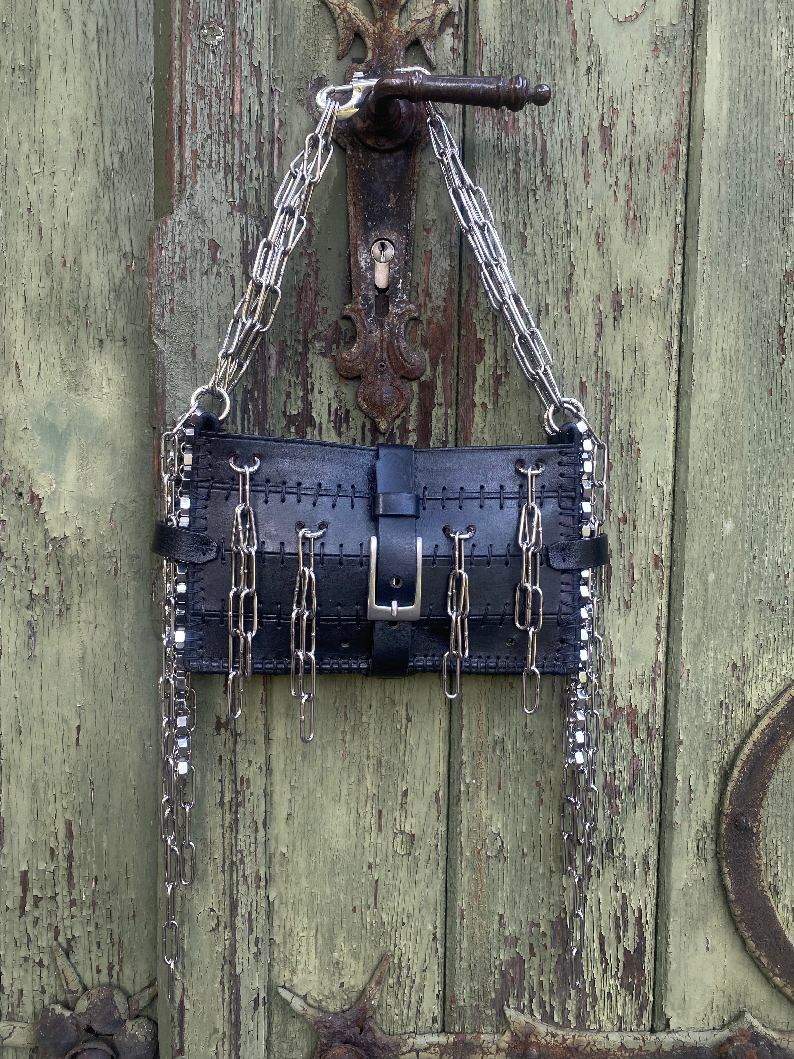 Handcrafted sustainable leather bag made from upcycled materials, featuring unique industrial chain details, hanging on an old vintage door. Made in Berlin by a one-woman business.