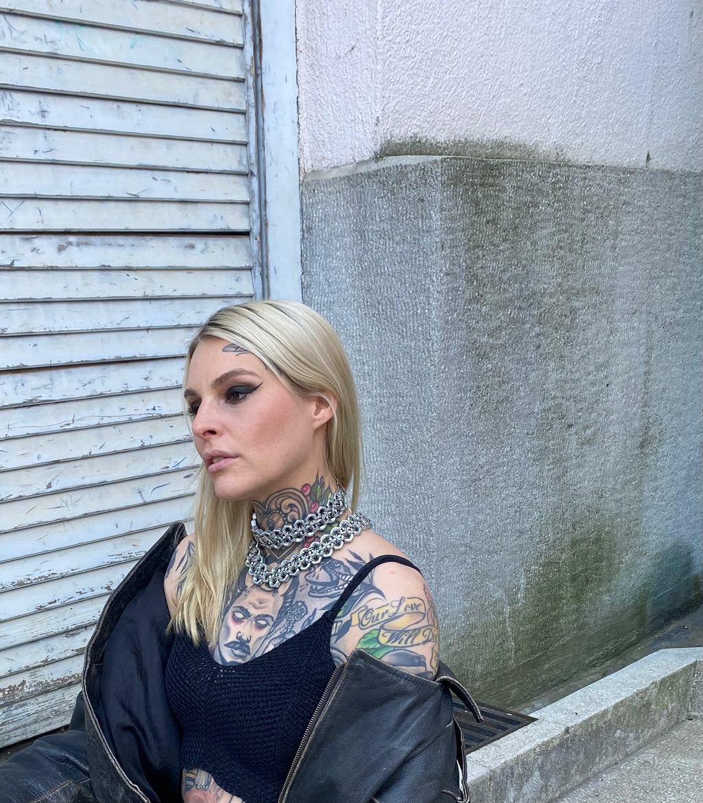Tattooed model wearing industrial heavy-metal chainmail choker necklaces made from stainless steel screws and chainmail, styled with a vintage leather jacket.