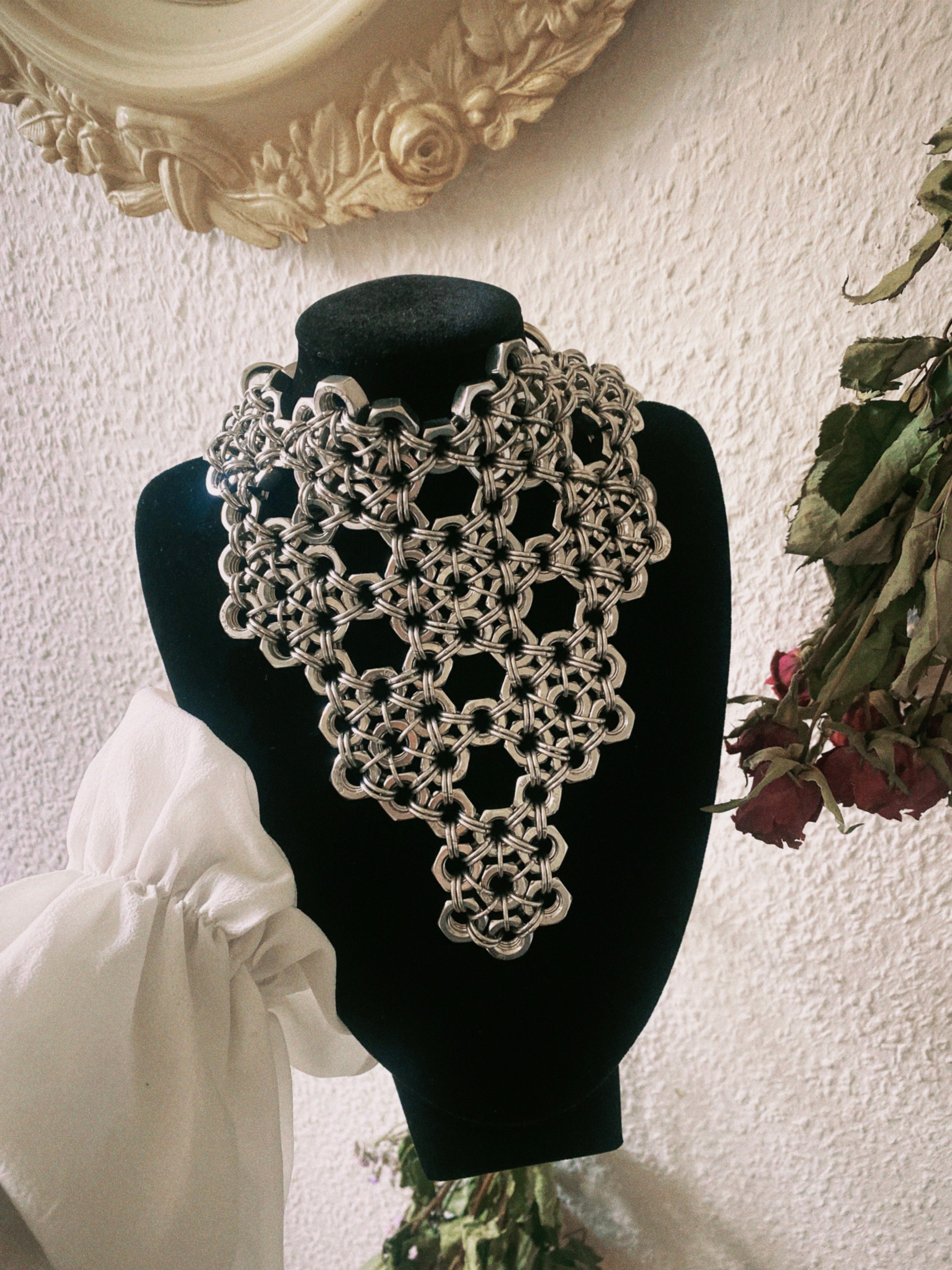 Super large industrial chainmail necklace displayed on a black necklace stand. Handmade stainless steel chainmail and industrial screws form a unique floral-inspired pattern, creating a bold statement piece.