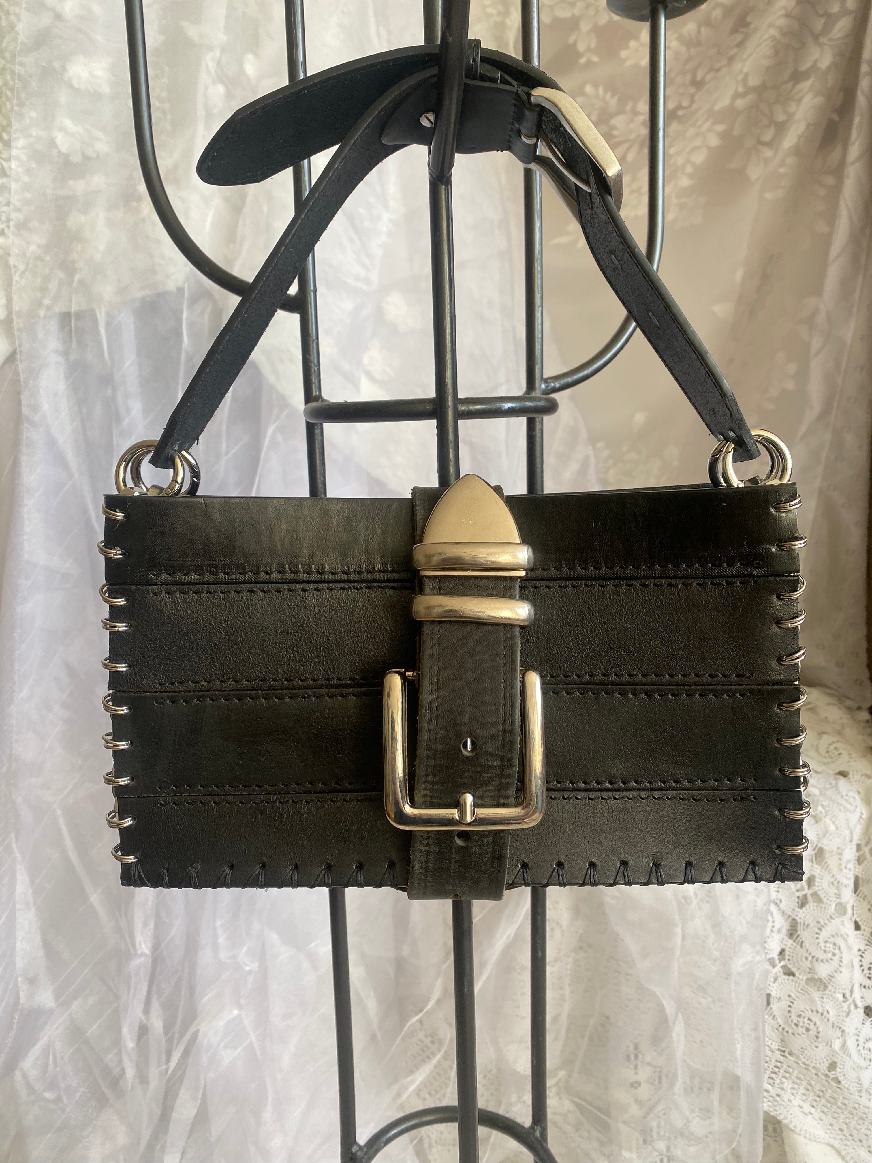 Statement piece upcycled leather handbag shown from the front view, hanging, where its handmade character comes through beautifully. Made from thick and durable sustainable leather material, photographed in front of vintage white lace.