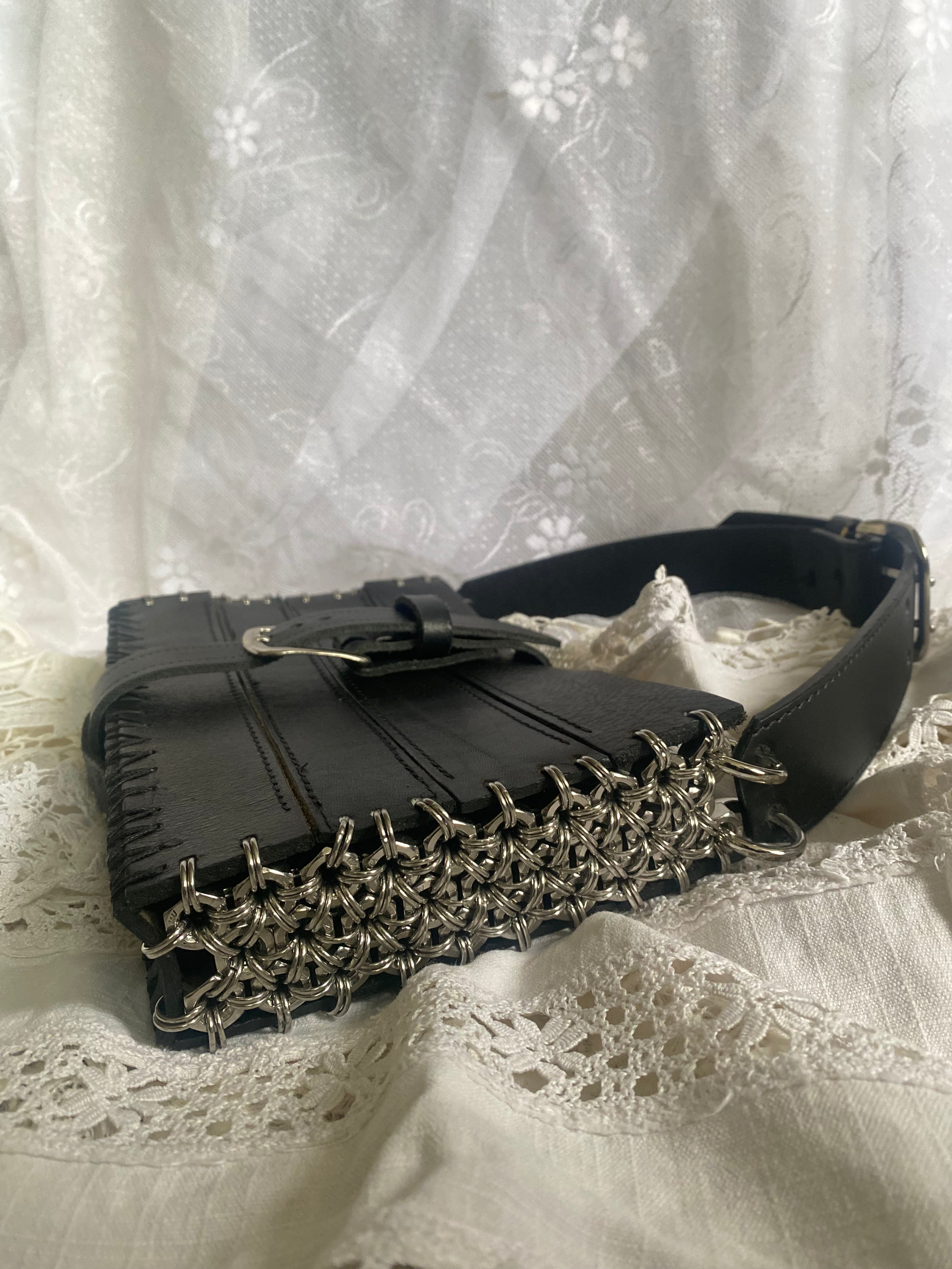 True sustainable leather handbag made from thick upcycled leather, lying on vintage Victorian-style lace. Features unique chainmail details on the sides, making it a bold statement piece in avant-garde fashion. Luxury-level craftsmanship for the alternative fashion scene.