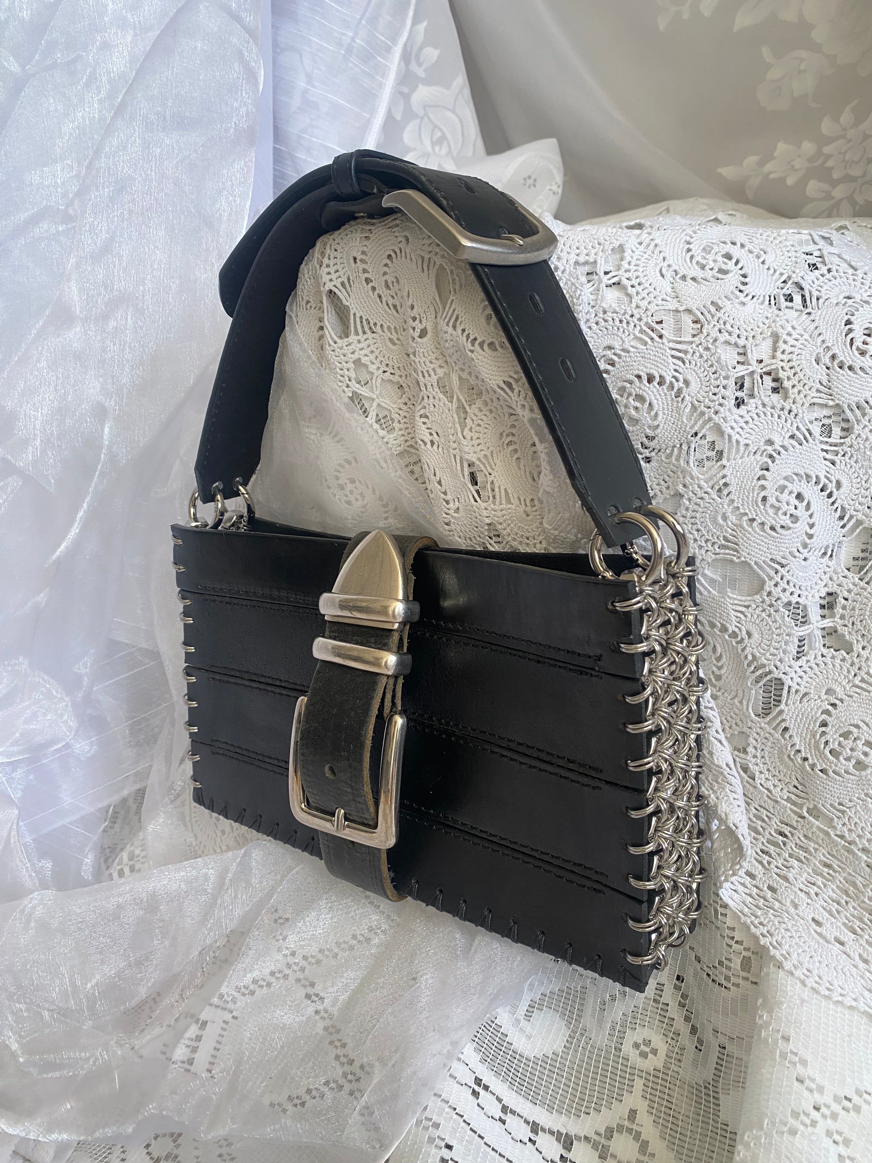 Black sustainable handbag made from upcycled leather with chainmail detail, wearable as a shoulder bag, displayed on white Victorian gothic aesthetic fabric.