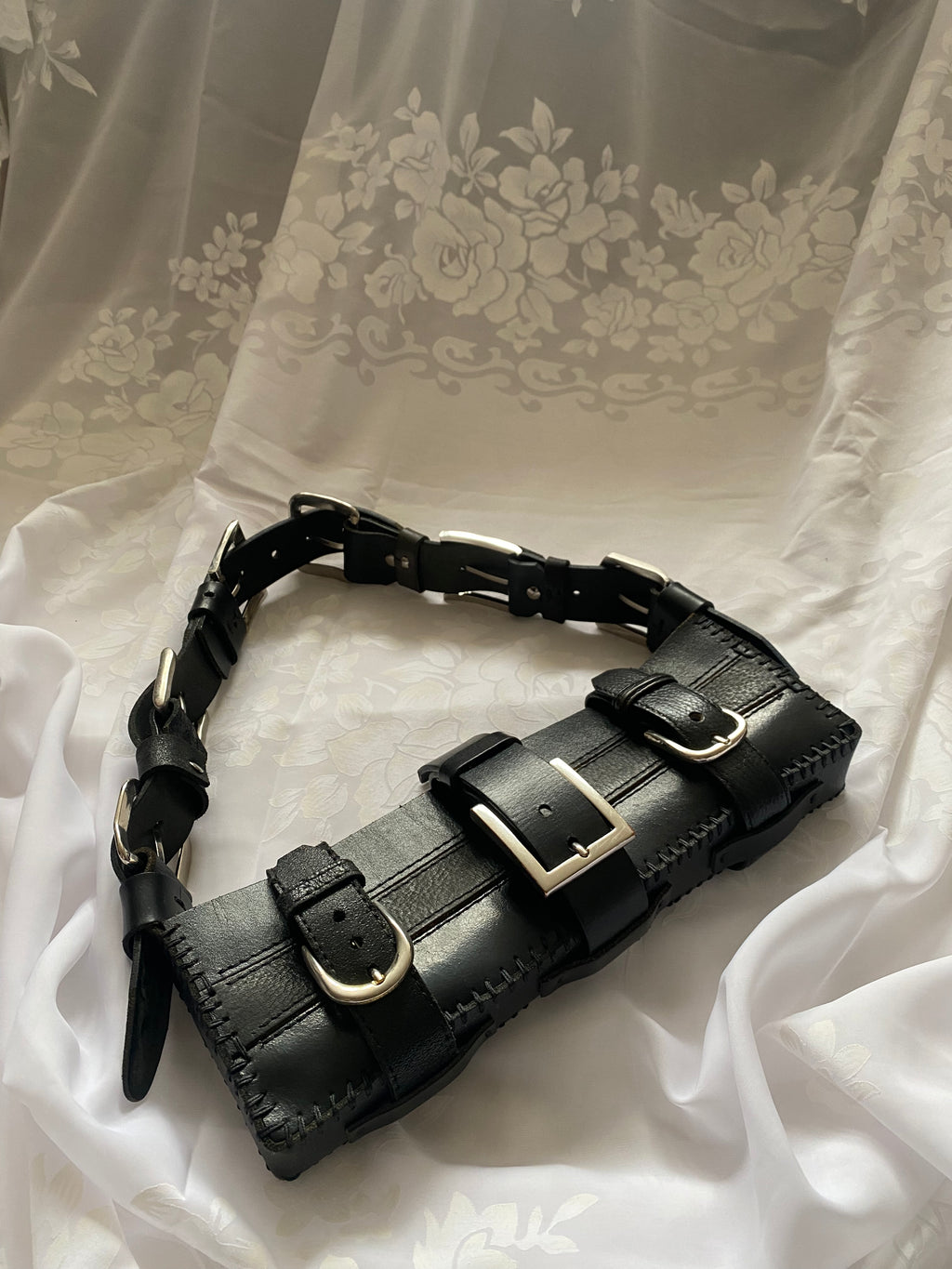 Upcycled leather handbag on white vintage tablecloth for a luxury gothic look, featuring a handle made of five belt buckles connecting the leather. Handmade, high-quality fashion accessory for a bold statement.