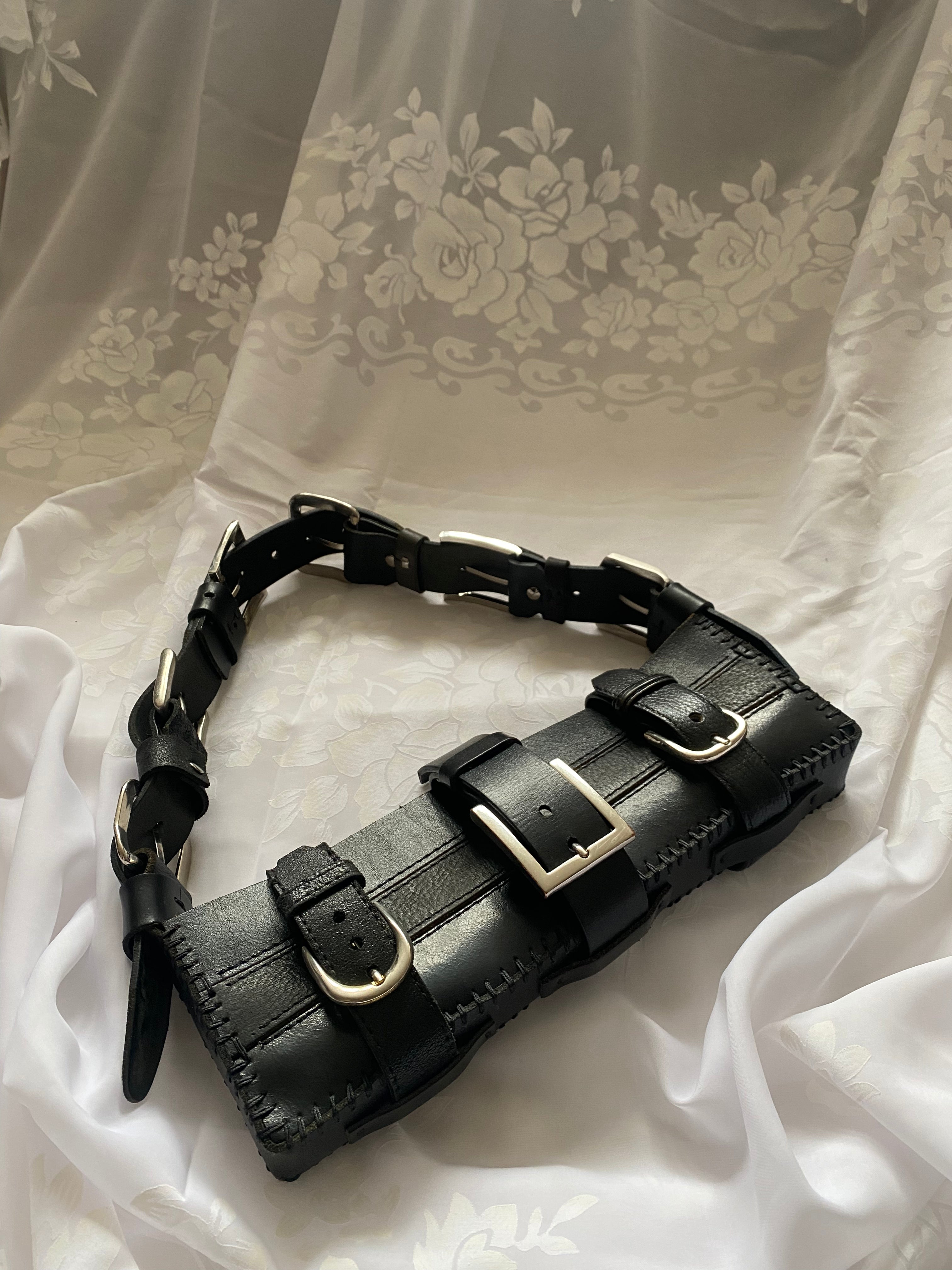 Upcycled leather handbag on white vintage tablecloth for a luxury gothic look, featuring a handle made of five belt buckles connecting the leather. Handmade, high-quality fashion accessory for a bold statement.