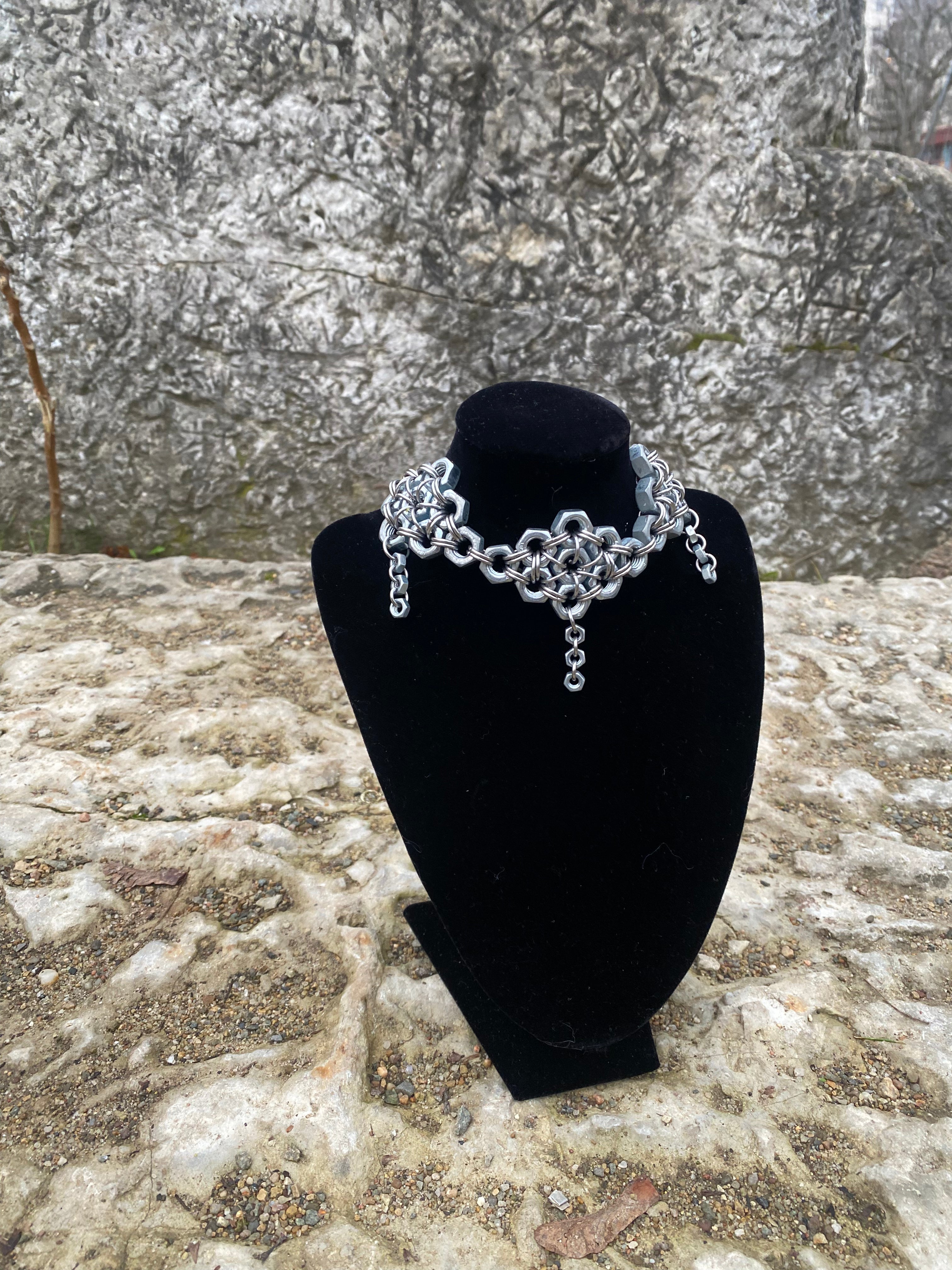 Silver unique chainmail necklace made from screws and rings in the name of industrial fashion made in Berlin on a black velvet stand against a stone background