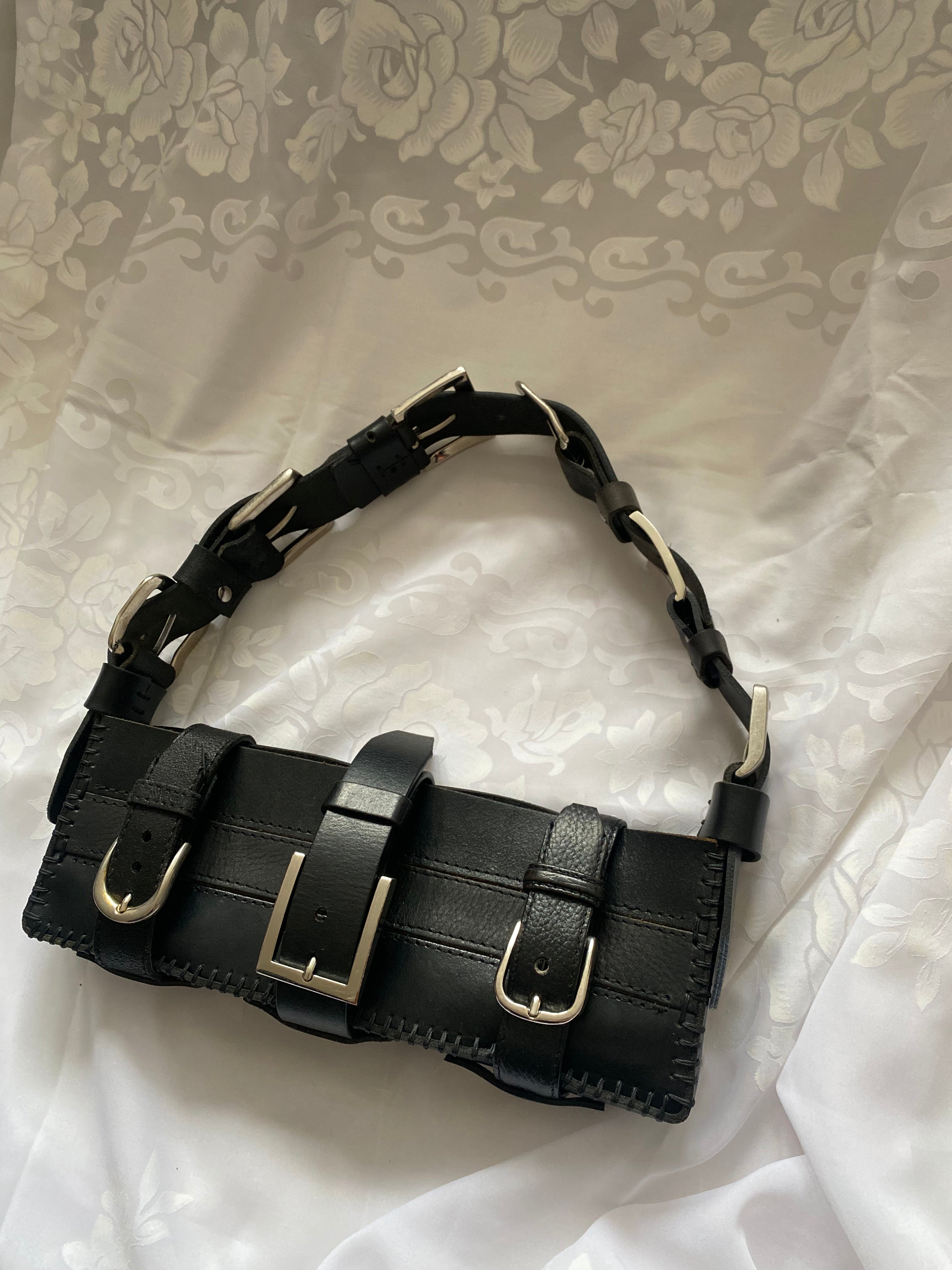 Sustainable black leather handbag on gothic Victorian-style fabric, featuring a unique belt-buckled handle and three belt-buckle closures. Longer than standard bags, handmade with luxury craftsmanship.
